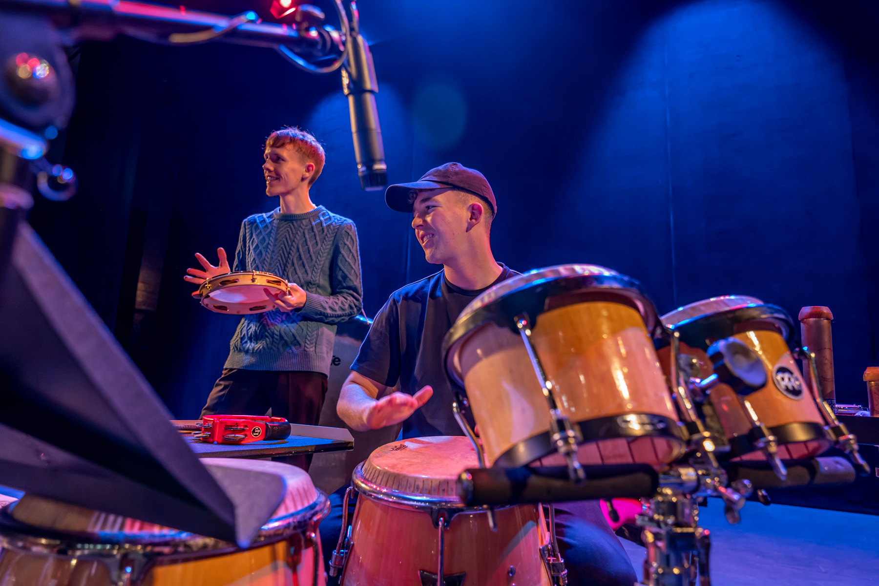 A male student sitting at a drum, rehearsing in a jazz orchestra performance.